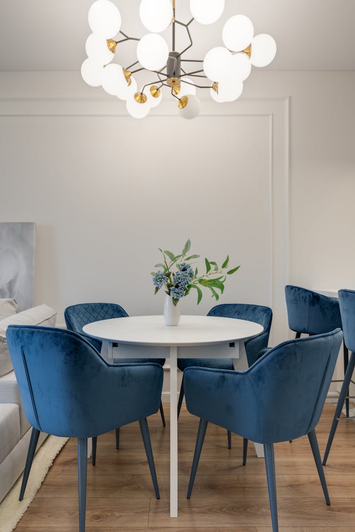 Elegant dining area featuring blue velvet chairs, round table, and stylish chandelier lighting.